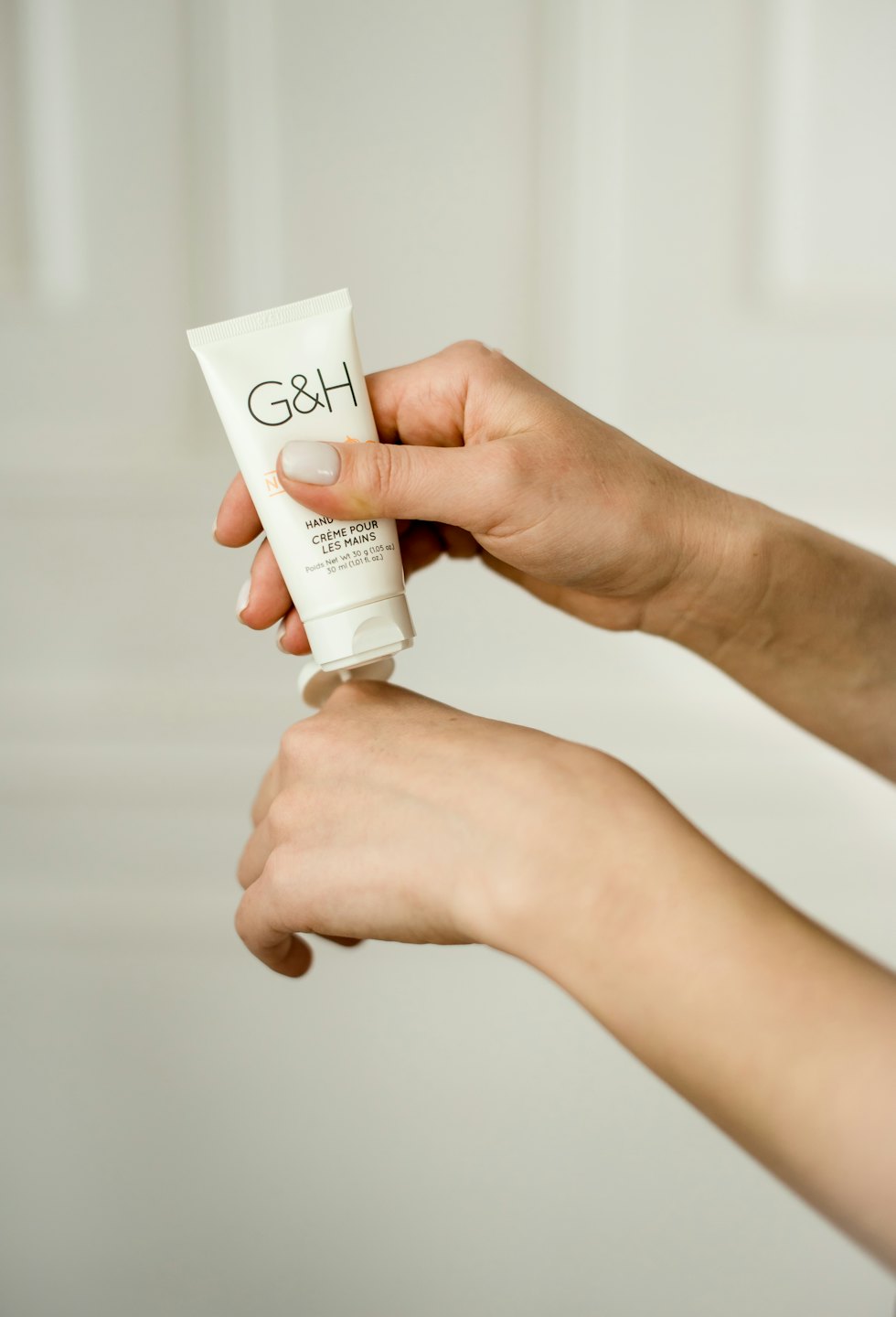 Hands applying skincare cream from a white tube.