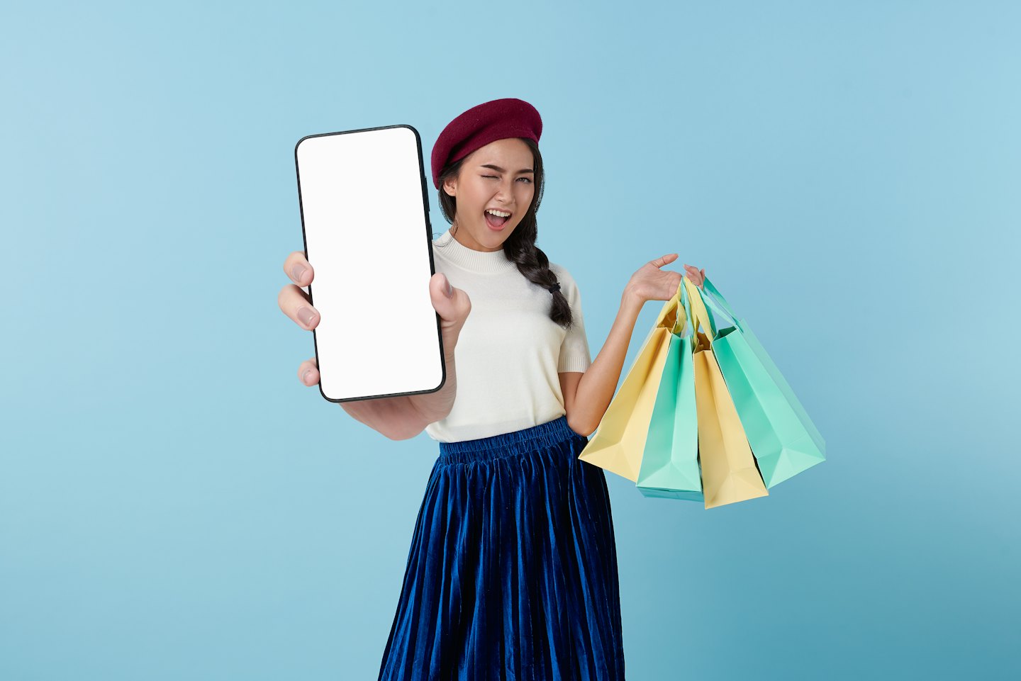 Woman in a red beret holds a smartphone and shopping bags.